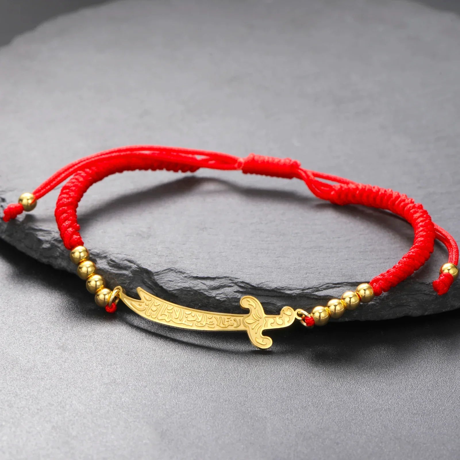 アリ・ズルフィカールのアラビア文字入り剣モチーフの赤いコードブレスレット（ゴールド）